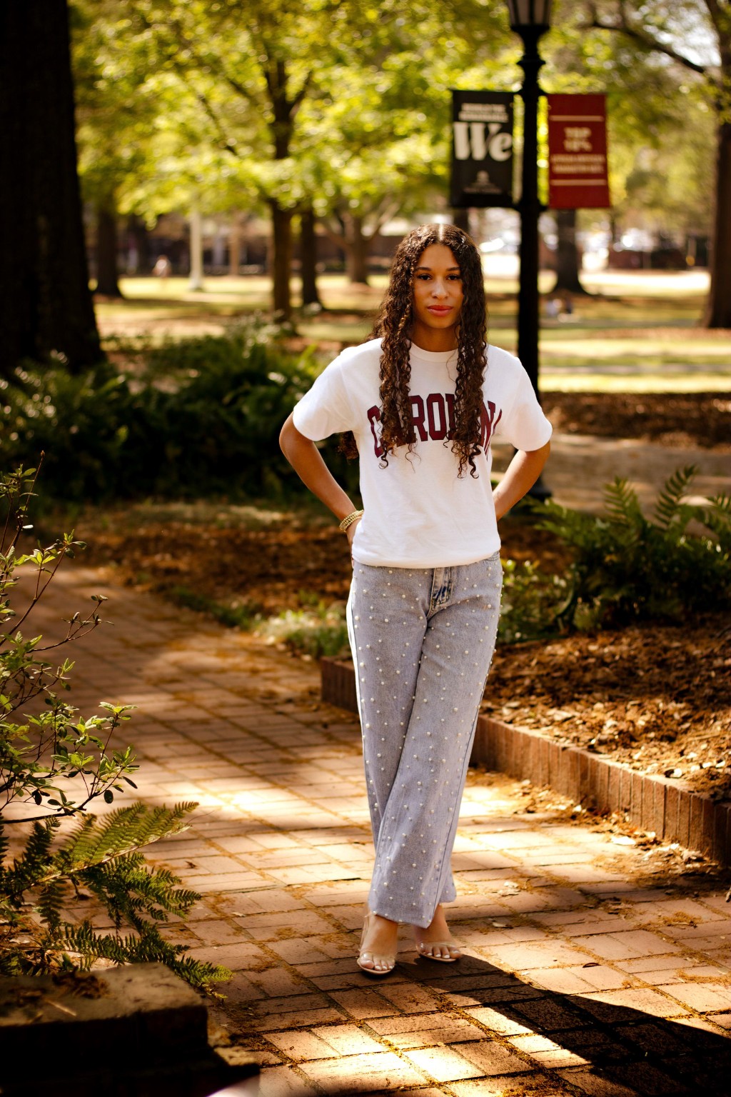 Layla walking through a sunlit campus setting in her Carolina shirt
