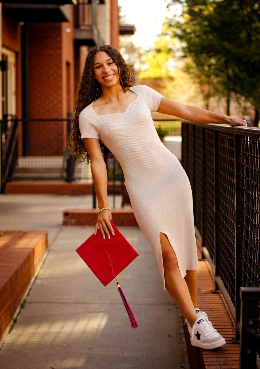 Layla posing in a white dress beside a railing with her graduation cap